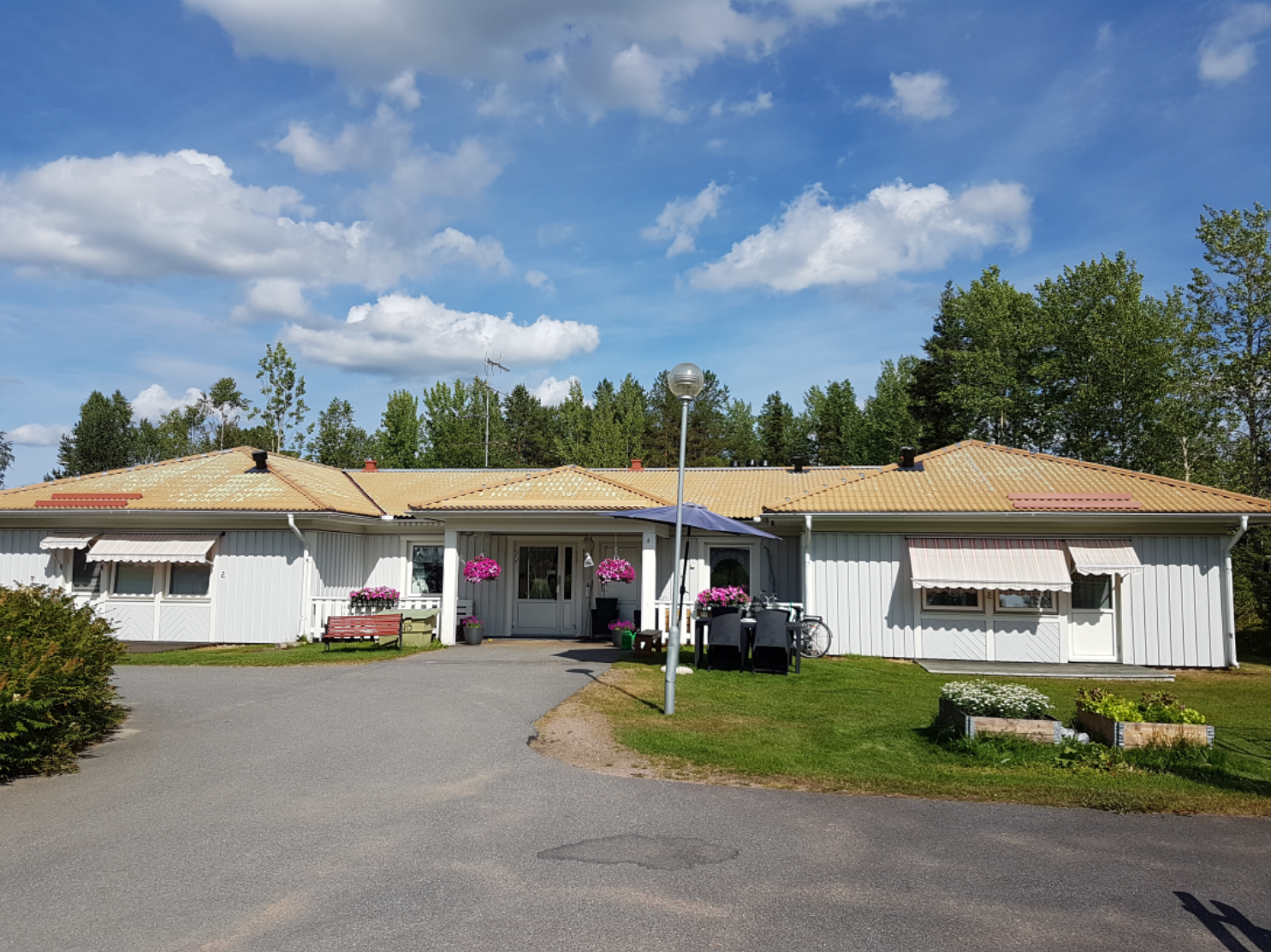 Åkerbärsgränds boende. Ingången kantas av gräsmatta, blommor, bord, stolar och bänkar.